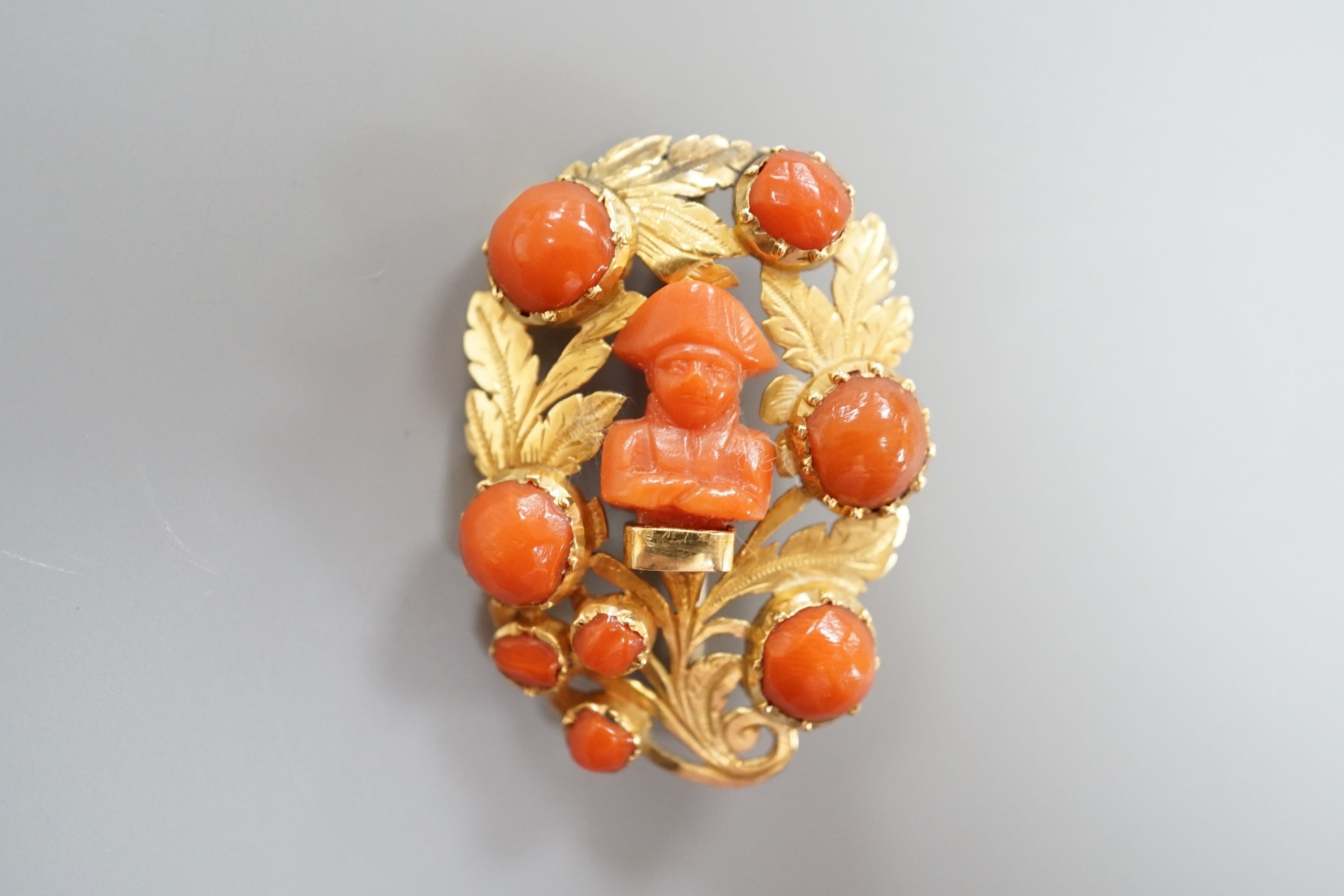 A 19th century yellow metal and coral set foliate brooch, the central motif carved as the bust of Napoleon, 37mm, gross weight 8.7 grams.